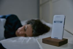Eine Frau schläft in ihrem Bett. Der CardioMessenger Smart ist in seiner Halterung auf dem Nachttisch.