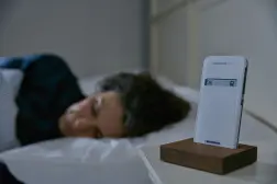 Eine Frau schläft in ihrem Bett. Der CardioMessenger Smart ist in seiner Halterung auf dem Nachttisch.